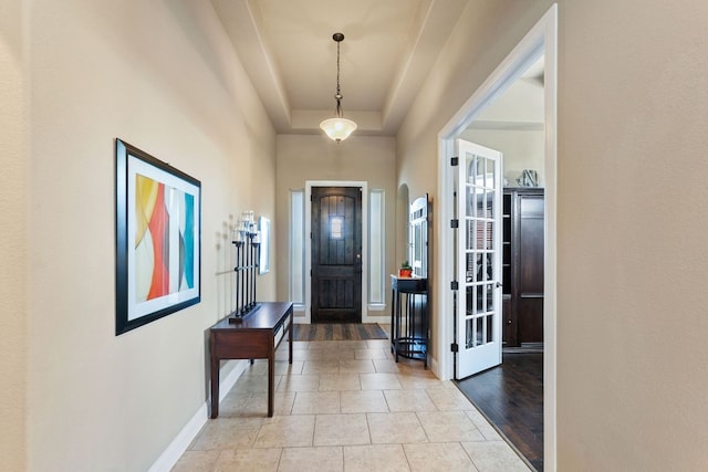 tiled entryway with a tray ceiling and baseboards