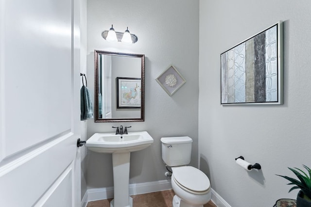 half bathroom featuring toilet, baseboards, and a sink