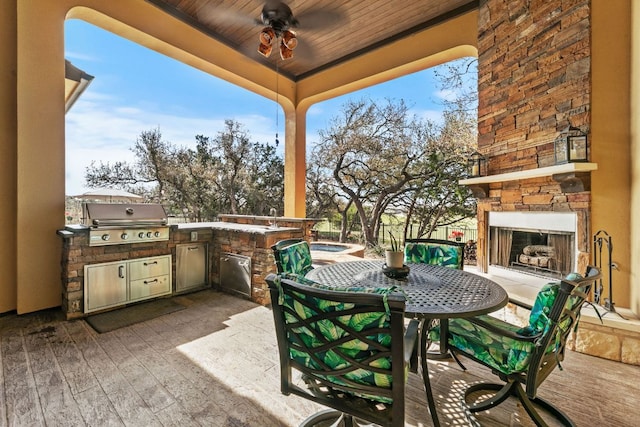 view of patio / terrace with fence, exterior kitchen, outdoor dining area, an outdoor stone fireplace, and grilling area