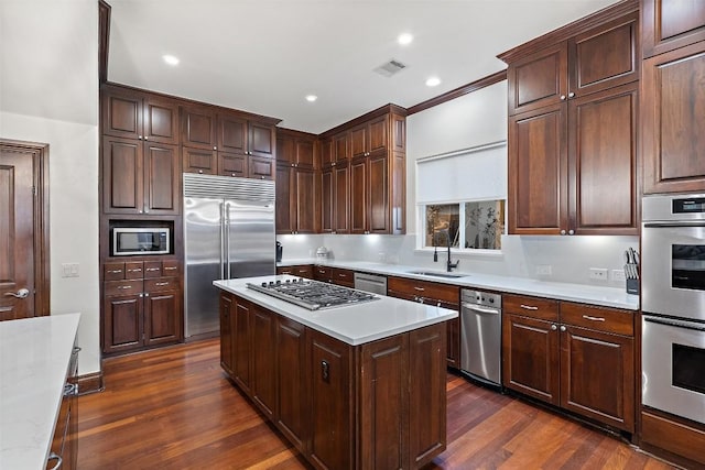 kitchen with visible vents, a sink, built in appliances, light countertops, and dark wood-style flooring