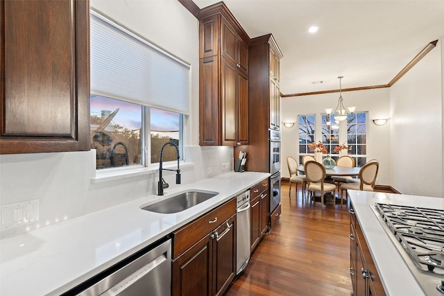 kitchen with a sink, decorative light fixtures, ornamental molding, stainless steel appliances, and dark wood-style flooring