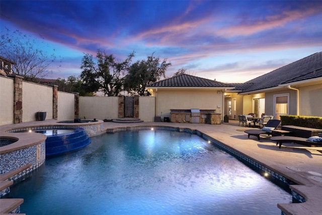 view of swimming pool with a patio, fence, a pool with connected hot tub, and an outdoor kitchen