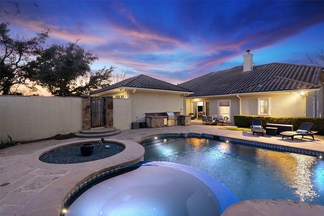 pool at dusk featuring area for grilling, a pool with connected hot tub, a gate, a patio, and fence