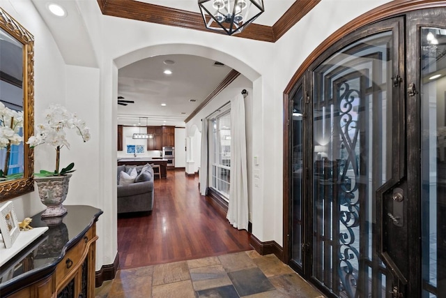 entryway featuring arched walkways, stone tile floors, crown molding, and baseboards