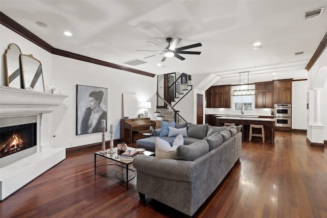 living area with dark wood finished floors, crown molding, visible vents, and a warm lit fireplace