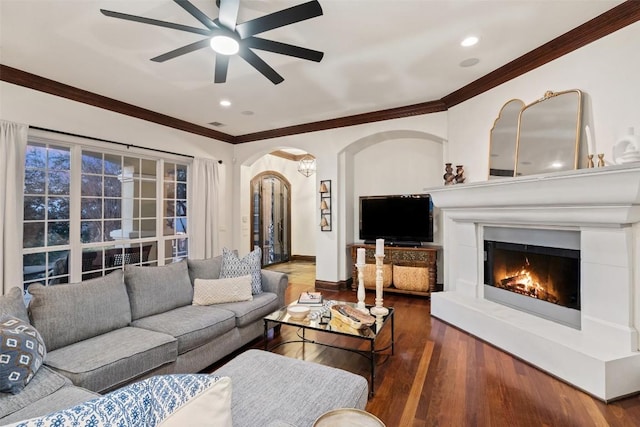 living area with a ceiling fan, baseboards, wood finished floors, arched walkways, and ornamental molding