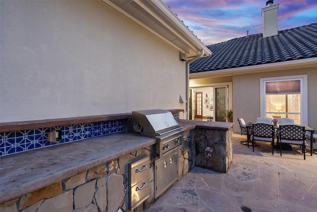 patio terrace at dusk with outdoor dining area, area for grilling, and an outdoor kitchen