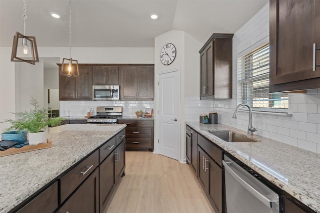 kitchen featuring dark brown cabinets, pendant lighting, light wood-style flooring, appliances with stainless steel finishes, and a sink