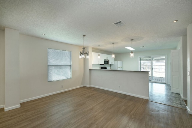 unfurnished living room with a textured ceiling, wood finished floors, visible vents, and baseboards