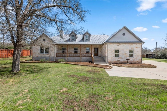 view of front facade featuring a front lawn, stone siding, fence, metal roof, and a chimney