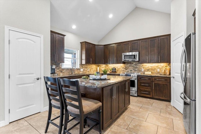 kitchen with stone countertops, tasteful backsplash, a kitchen island, stainless steel appliances, and dark brown cabinetry