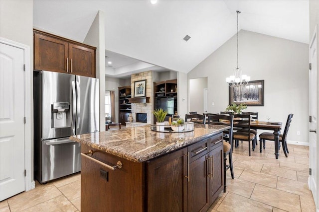 kitchen featuring a kitchen island, dark brown cabinetry, decorative light fixtures, stone counters, and stainless steel refrigerator with ice dispenser