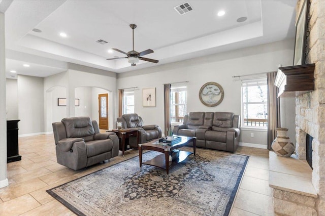 living area with a stone fireplace, a tray ceiling, arched walkways, and visible vents