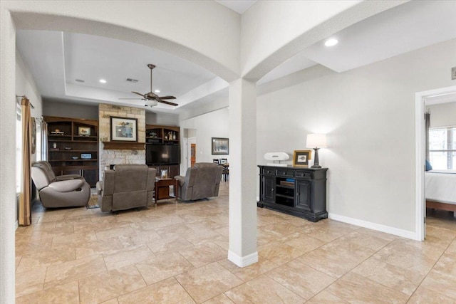 living room with ceiling fan, baseboards, a tray ceiling, recessed lighting, and arched walkways