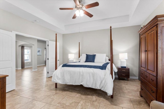 bedroom with arched walkways, ceiling fan, baseboards, and a tray ceiling