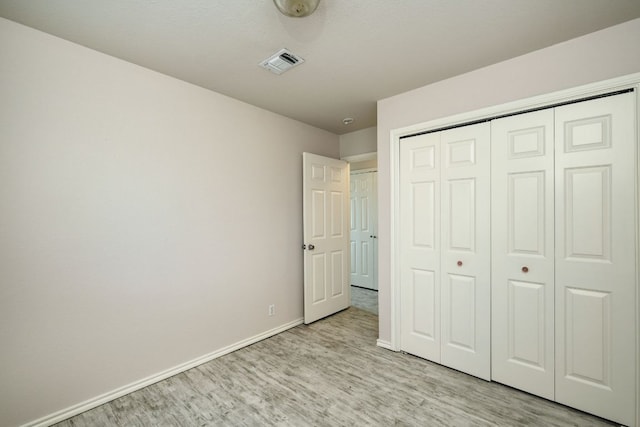 unfurnished bedroom featuring visible vents, baseboards, a closet, and wood finished floors