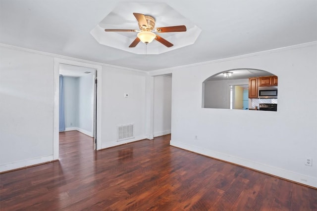 spare room with a tray ceiling, wood finished floors, visible vents, and ceiling fan