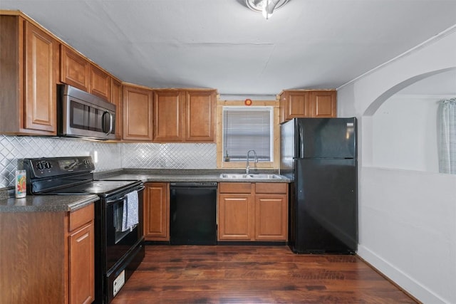 kitchen featuring dark countertops, backsplash, dark wood-type flooring, black appliances, and a sink