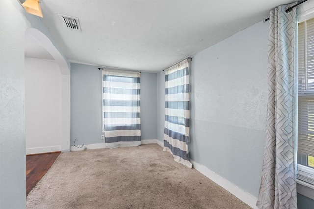 carpeted empty room featuring arched walkways, visible vents, and baseboards