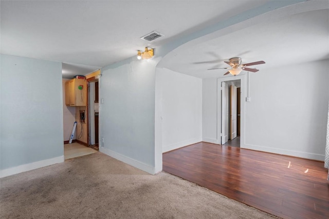 unfurnished living room with visible vents, wood finished floors, arched walkways, baseboards, and ceiling fan