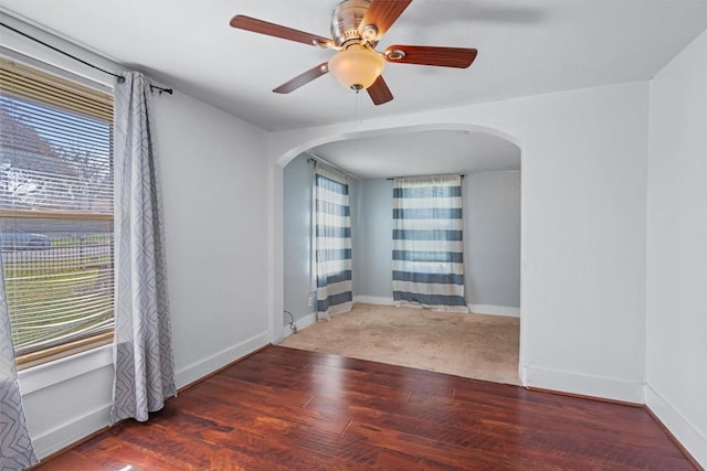 spare room with wood finished floors, arched walkways, and baseboards