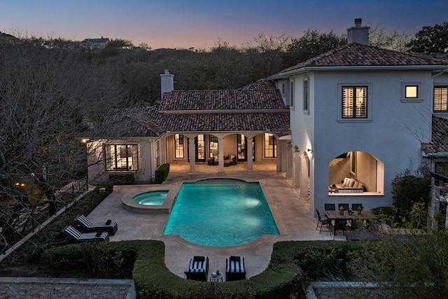 back of property with stucco siding, a patio area, a pool with connected hot tub, and a chimney