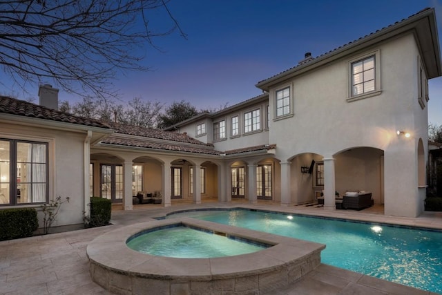 back of house at dusk featuring a patio area, french doors, an in ground hot tub, and stucco siding