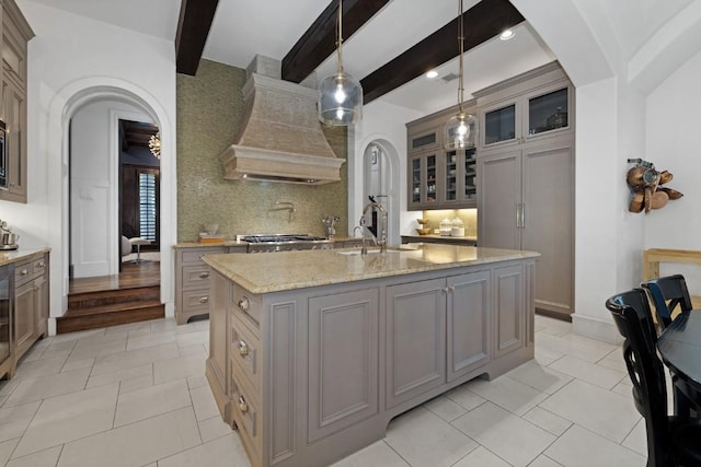 kitchen with backsplash, light stone countertops, custom range hood, arched walkways, and a sink