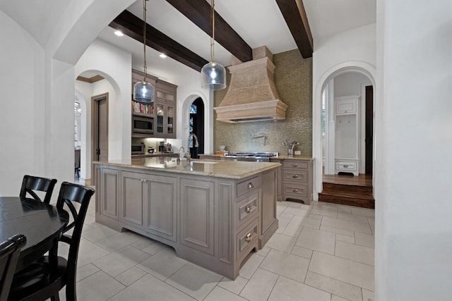 kitchen featuring stainless steel microwave, gray cabinetry, custom range hood, arched walkways, and a sink