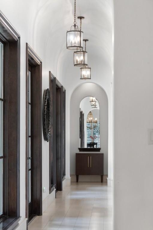 hall featuring arched walkways, lofted ceiling, an inviting chandelier, and light tile patterned flooring