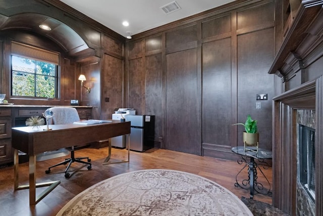 office space with a fireplace, a decorative wall, wood finished floors, and visible vents