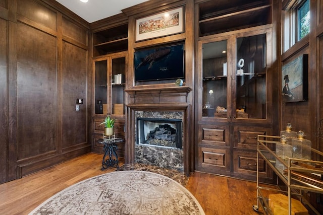 living area with built in features, a premium fireplace, wood finished floors, and wood walls