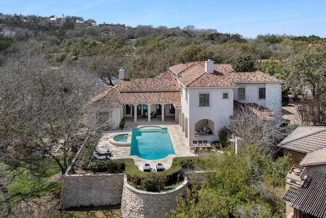 rear view of property featuring a wooded view, a tiled roof, stucco siding, a chimney, and a patio