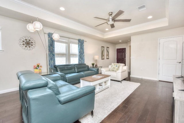 living room featuring a tray ceiling, dark wood-type flooring, visible vents, and ceiling fan