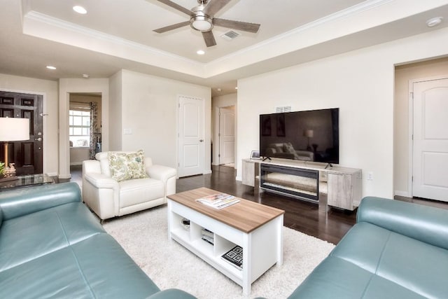 living room featuring wood finished floors, a ceiling fan, visible vents, crown molding, and a raised ceiling