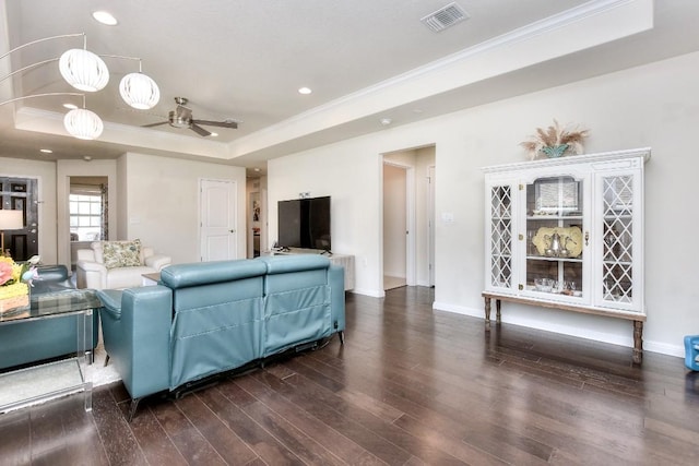 living room featuring a tray ceiling, visible vents, dark wood finished floors, and ornamental molding