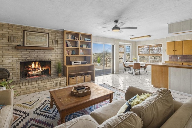 living room with tile patterned flooring, a brick fireplace, a textured ceiling, and a ceiling fan