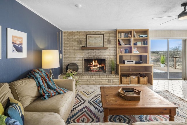 living room featuring a brick fireplace, a textured ceiling, a ceiling fan, and ornamental molding