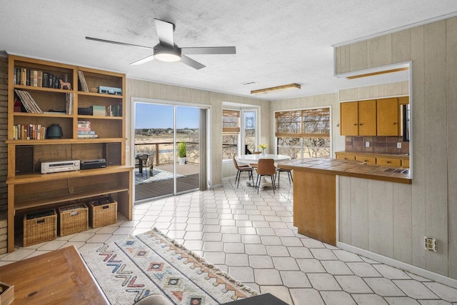 kitchen with a ceiling fan, a textured ceiling, wooden walls, a peninsula, and tile counters