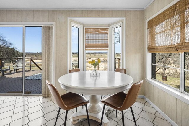 dining space featuring crown molding, a healthy amount of sunlight, baseboards, and wood walls