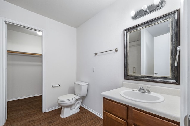 bathroom with vanity, wood finished floors, baseboards, a spacious closet, and toilet