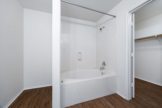 bathroom with baseboards, a walk in closet, bathtub / shower combination, and wood finished floors