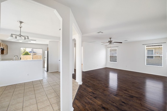 unfurnished living room with light wood-style flooring, ceiling fan with notable chandelier, visible vents, and a sink