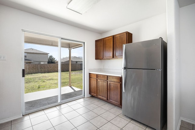 kitchen with light tile patterned floors, brown cabinets, light countertops, and freestanding refrigerator