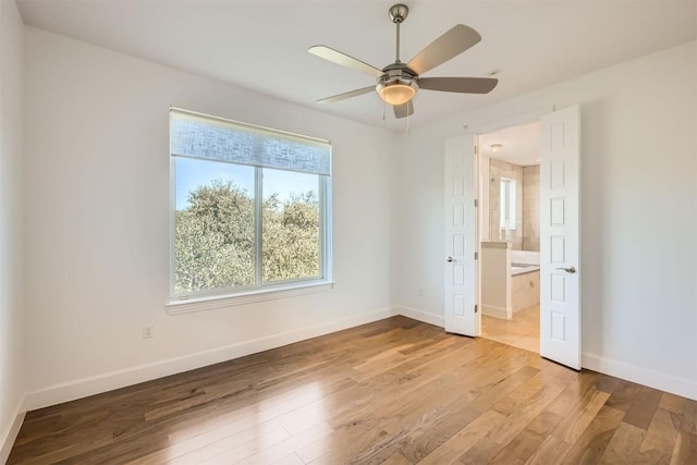 unfurnished bedroom with ensuite bathroom, baseboards, and wood finished floors