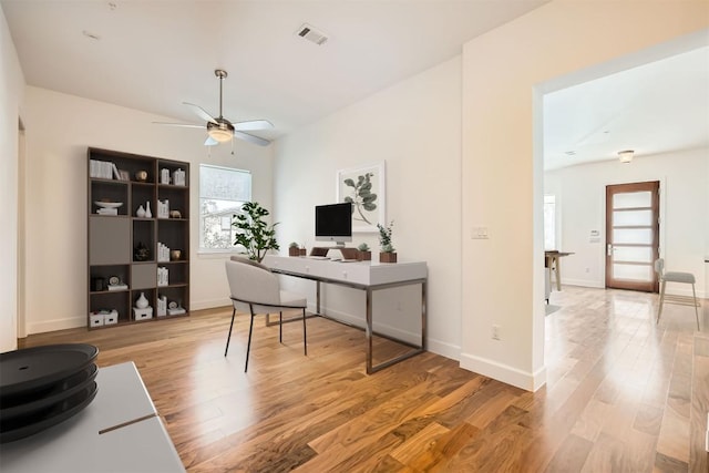 home office featuring visible vents, baseboards, light wood-type flooring, and a ceiling fan