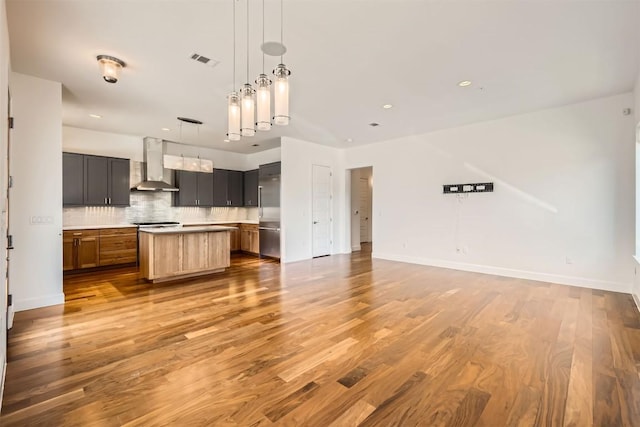 kitchen with wood finished floors, visible vents, open floor plan, wall chimney range hood, and tasteful backsplash