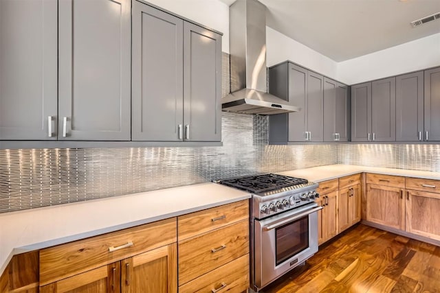 kitchen featuring visible vents, dark wood-style flooring, high end stove, wall chimney exhaust hood, and backsplash