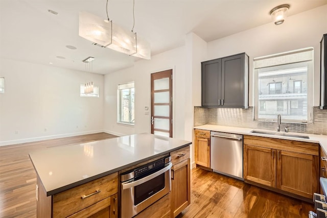 kitchen with a sink, decorative light fixtures, tasteful backsplash, wood finished floors, and appliances with stainless steel finishes