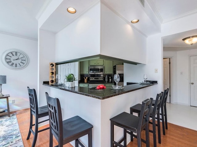 kitchen featuring green cabinets, a kitchen bar, ornamental molding, appliances with stainless steel finishes, and a peninsula